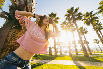 young smiling woman tilting her head against a background of palms and sunset looking into the sunset