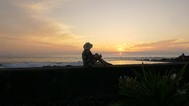 A woman sitting on a seawall taking in a beautiful sunset