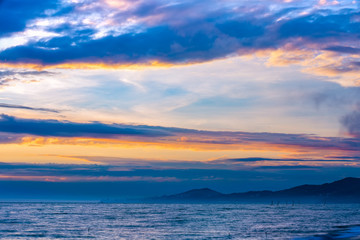 High clouds and fog on the coast, the sun is hidden behind the clouds, on the shoreline are visible the houses of the city on the hills. Beautiful colorful sunset on the Black Sea, Sochi, Russia.