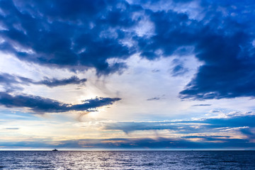 Obraz premium The blue beautiful landscape of the sky with graceful clouds blockaded the bright sun over the sea, the ship in the distance on the horizon. Beautiful colorful sunset on the Black Sea, Sochi, Russia.
