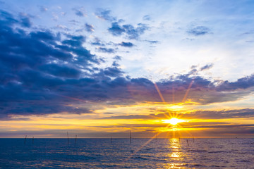 The bright rays of the yellow sun illuminates the sky with thick blue clouds and the evening sea on the shore. Beautiful colorful sunset on the Black Sea, Sochi, Russia.