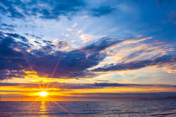 The bright rays of the yellow sun illuminates the sky with thick blue clouds and the evening sea on the shore. Beautiful colorful sunset on the Black Sea, Sochi, Russia.