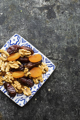 Blue white painted square plate full of walnuts and dried fruits: walnut, prunes, dates, dried apricots on a dark gray background. Top View.