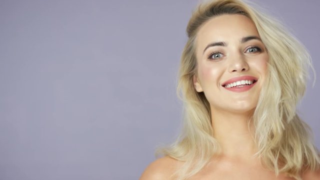 Headshot of positive beautiful female model with blonde hair looking at camera and posing in studio.
