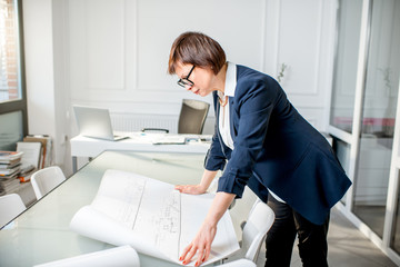 Elegant senior woman architect working with drawings standing in the white office