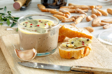 Chicken liver pate jar covered with melted butter and decorated with bay leaves and black and red pepper.