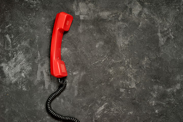 The red bright handset from a classic rotary dial phone on a black rustic cement background, top...