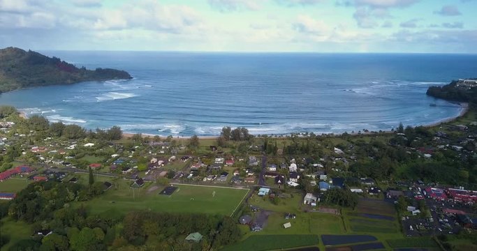 Kauai Hawaii aerial slow move away sandy beach cove and vacation town over rice fields.