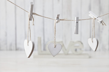 The wooden heart shape on the rope is attached with a clothespin. A concept for the Valentine's Day,  wedding,  engagement. Close-up, selective focus, shallow depth of field. White wooden background 