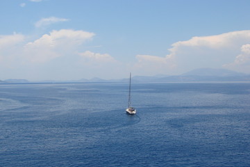 Marine landscape with a lonely yacht in the middle of the Aegean Sea on the background of a cloudy blue sky.