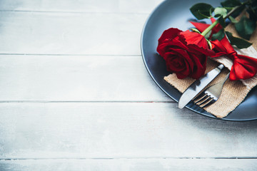 Festive table setting for Valentine's Day with fork, knife and rose on a white wooden table. Space for text. Top view.