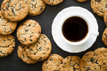 Cup of black coffee and cookies with chocolate pieces on the dark table. Resting and enjoying time with coffee and sweets. Drink and snack concept.
