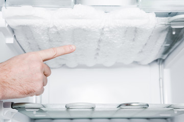 Man's hand pointing to the frozen ice in the empty freezer. Problem and solution concept.