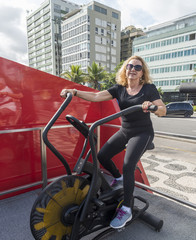 Fototapeta na wymiar Older woman (70-79) exercising on biking machine at open air gym in Rio de Janeiro, Brazil
