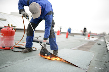 Flachdach Reparatur: Dachdecker verschweißt Dachabdichtung. Dachsanierung mit Gasbrenner. Immer Feuerlöscher vorhalten. - obrazy, fototapety, plakaty