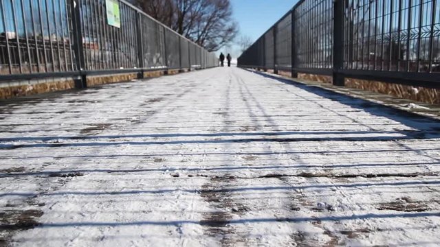 2 people walking on snowy bridge on sunny winter day