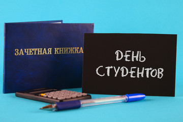 A blue book with an inscription in Russian - a student's record book. Pen, calculator on a blue background. Inscription in Russian - Students Day.