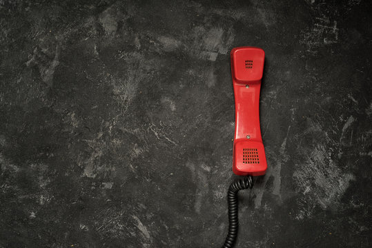 Red retro styled phone handset and black cement background