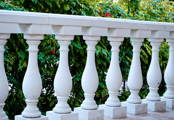 White marble columns in a row, parapet, fence, against the background of green flowering bushes,...