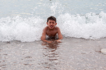 Young boy enjoying his summer vacation, swimming, and playing in the sea with waves splashing over him 