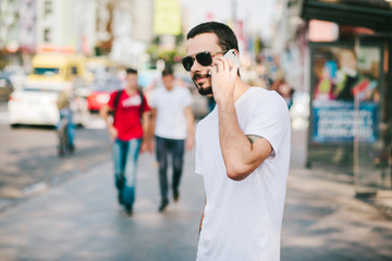 Handsome hipster modern man with beard walking in town and calling on mobile phone