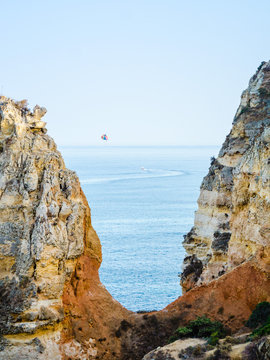 Parasailing, also known as parascending or parakiting at the coasts of the Algarve in Lagos, Portugal. Surrounded with yellow, orange limestones.