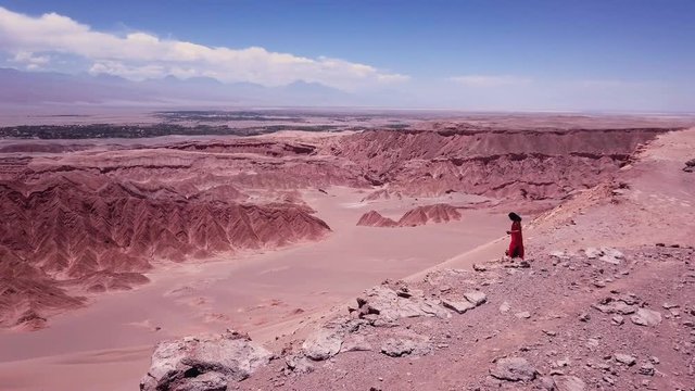 Woman wearing a red dress standing over the edge of a sand desert, Dead Valley, Chile. Aerial shot, 4k