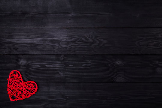 Red heart lies on a wooden black background, top view with copy space.