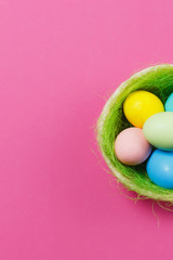 Vertical six colorful pastel painted Easter eggs in basket with green grass isolated on pink background. Happy Easter concept. Copy space for advertisement. With place for text. Top view on eggs.