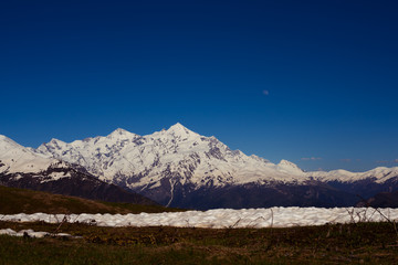 Fototapeta premium Pale moon rises over the snow-covered mountain ridge