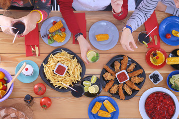 Top view of group of people having dinner together while sitting at wooden table. Food on the table. People eat fast food.