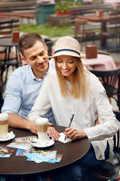 Travel. Beautiful Couple Writing Postcards Sitting At Cafe Table