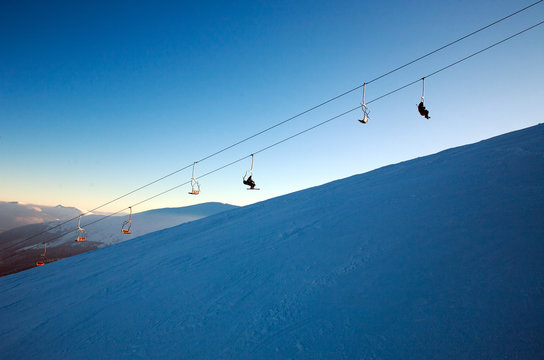 Ski lift in winter snowy landscape in mountains on blue sky background