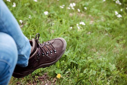 Horisontal image of crossed female legs wearing Alpine Touring Randonee Boots on woman feet in green mountain field.