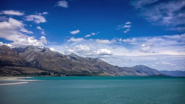  Time lapse at the remote alpine place of Kinloch in New Zealand with the beautiful serene waters of lake Wakatipu and the clouds rushing on top of the mountain on a fairly windy day.