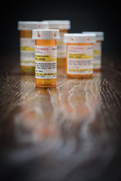 Variety of Non-Proprietary Prescription Medicine Bottles on Reflective Wooden Surface.