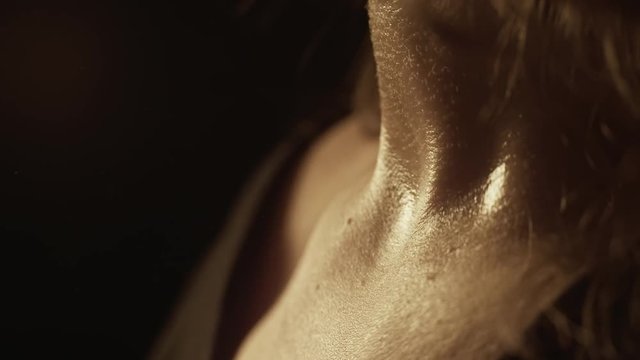 Close-up of a WOMAN applying perfume on her neck. Dim light emphasizes skin texture and sensuality.