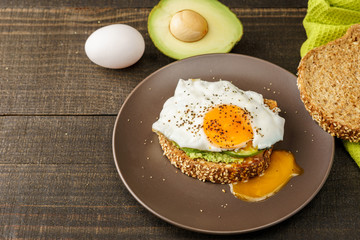 sandwich with avocado and a fried egg on a brown plate on a rustic wood and table bread on green kitchen towel.