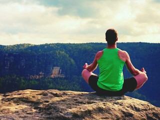 Man on top of mountain in yoga pose. Exercise yoga on edge with a breathtaking view