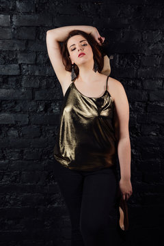 plus size model in a gold blouse and black jeans on a brick loft background.