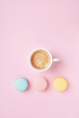 Cake macaron and cup of coffee on pastel pink background top view. Cozy morning breakfast. Fashion flat lay. Sweet macaroons.