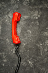 The red bright handset from a classic rotary dial phone on a black rustic cement background, top...