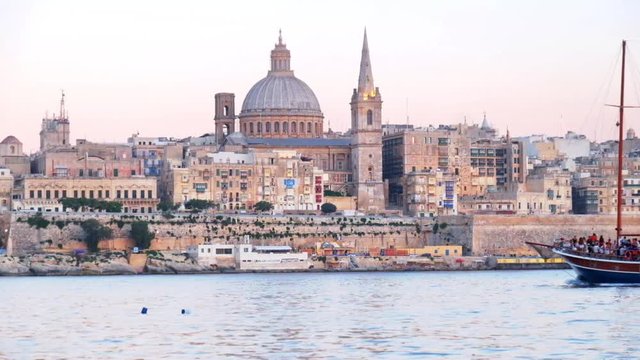 Fernandes malta ship in romantic sunset cruise along St. Paul's Bay of Malta Marsamxett Harbour with the view on Valletta St. Paul's Cathedral and belltower at the Evening time, Malta