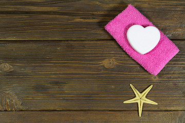 Soap in the shape of a heart on a pink towel. Wooden background