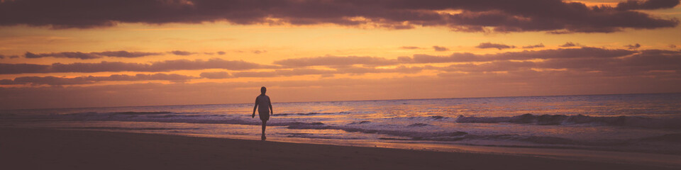 Some person is walking along the beach at sunrise. Banner photography format. - Powered by Adobe