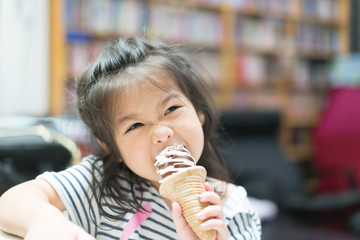 Happy Little asian girl eating soft cream or ice cream and she sit on sofa in living room.