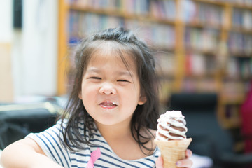 Happy Little asian girl eating soft cream or ice cream and she sit on sofa in living room.