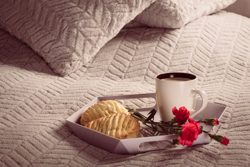 Tray with coffee, flower and cookie with apple, is lay on soft overlay on bed.