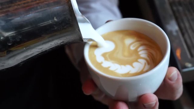 Barista pouring milk in cappuccino and doing latte art in coffee shop.