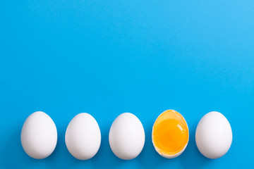 White eggs is laying in row, one of them is bisected and shows yolk.